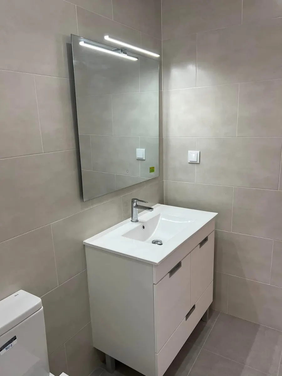 Depois da obra: móvel de lavatório branco com gaveta, espelho com luz e paredes em cerâmica.