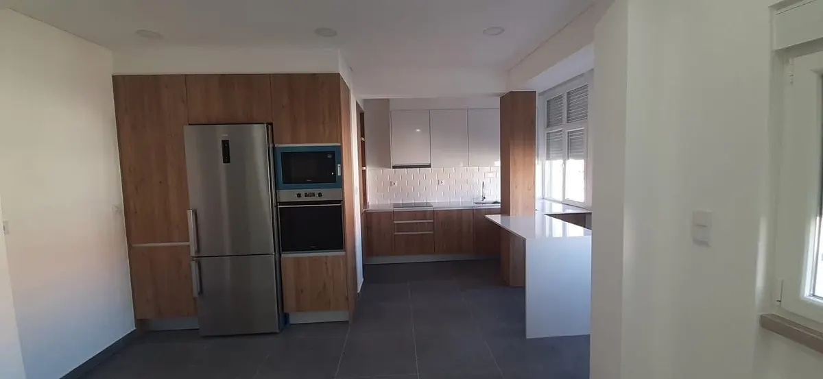 Cozinha remodelada com colunas em tom de carvalho, azulejo metro e península branca, depois da obra.