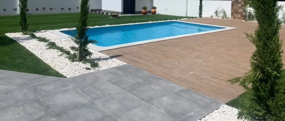 Piscina com deck, relvado e gravilha branca, com o anexo ao fundo, depois da obra.