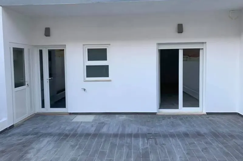 Fachada branca das traseiras com portas envidraçadas e pavimento cerâmico do pátio, depois da obra.