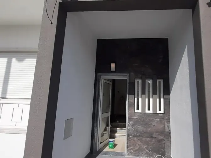 Entrada do prédio depois da remodelação, com pórtico cinzento e revestimento escuro junto à porta.