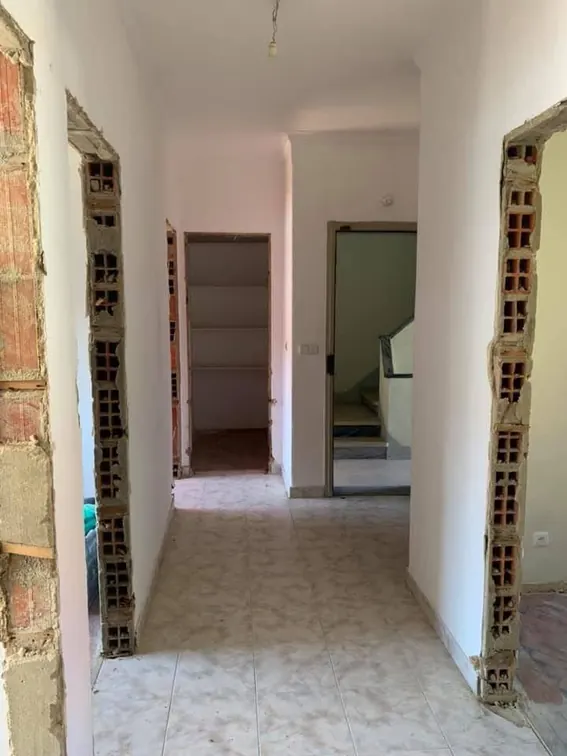 Corredor em demolição antes da remodelação, com tijolo à vista e pavimento cerâmico antigo.