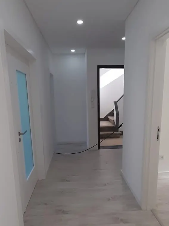 Corredor depois da remodelação, com pavimento laminado, teto com focos embutidos e portas brancas.