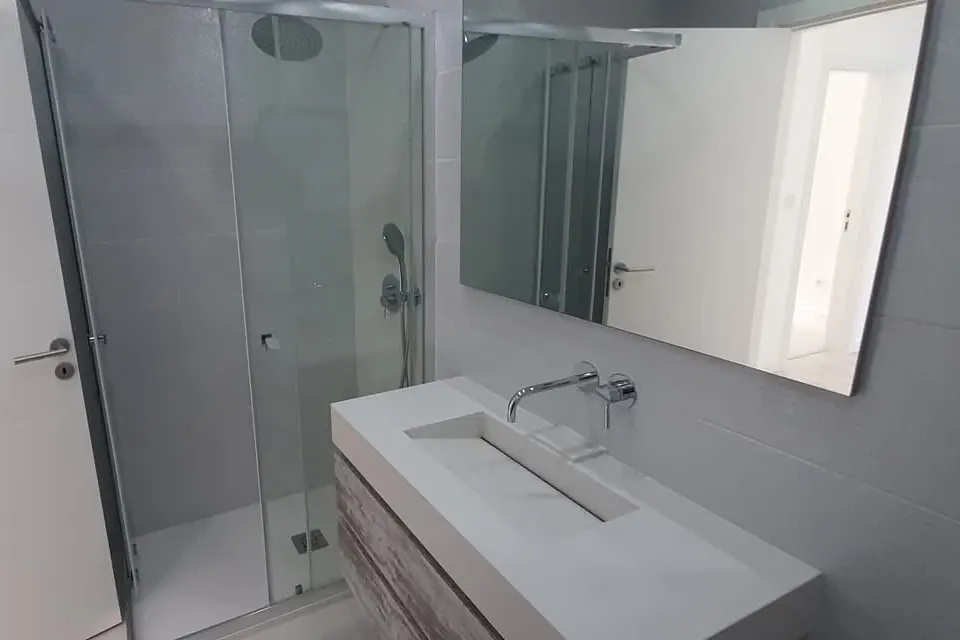 Casa de banho depois da remodelação, com resguardo de vidro, lavatório suspenso e espelho largo.